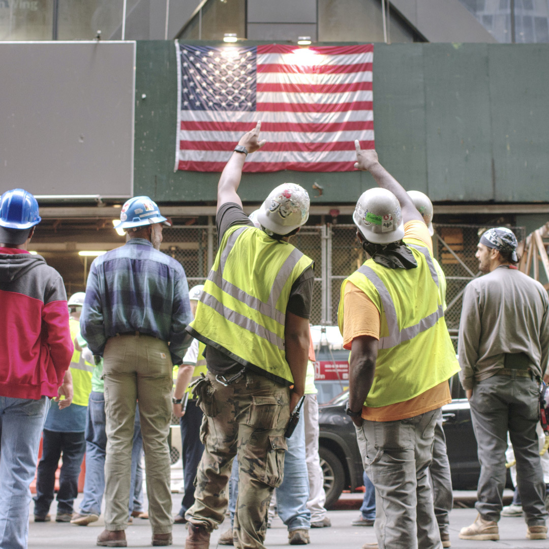 Construction workers looking at American flag.