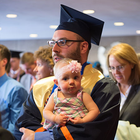 student veteran graduating while holding his baby.