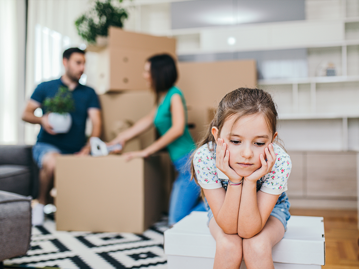 A sad daughter sitting as her parent unpack boxing from moving. 
