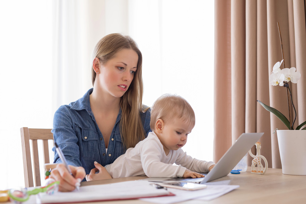 Mom trying to work remotely with baby calling on her laptop.