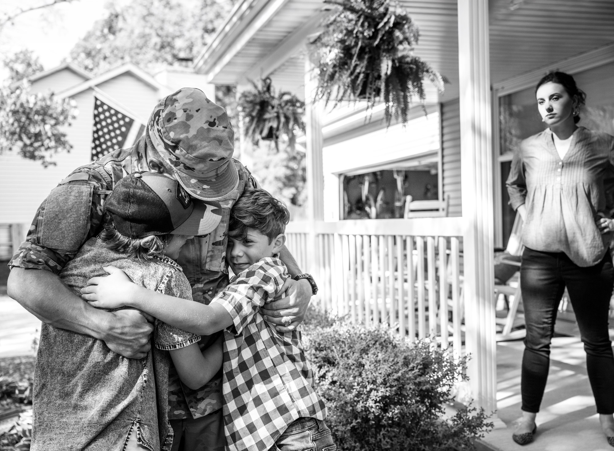 Military spouse watching her husband in uniform hugging their kids coming back from overseas.