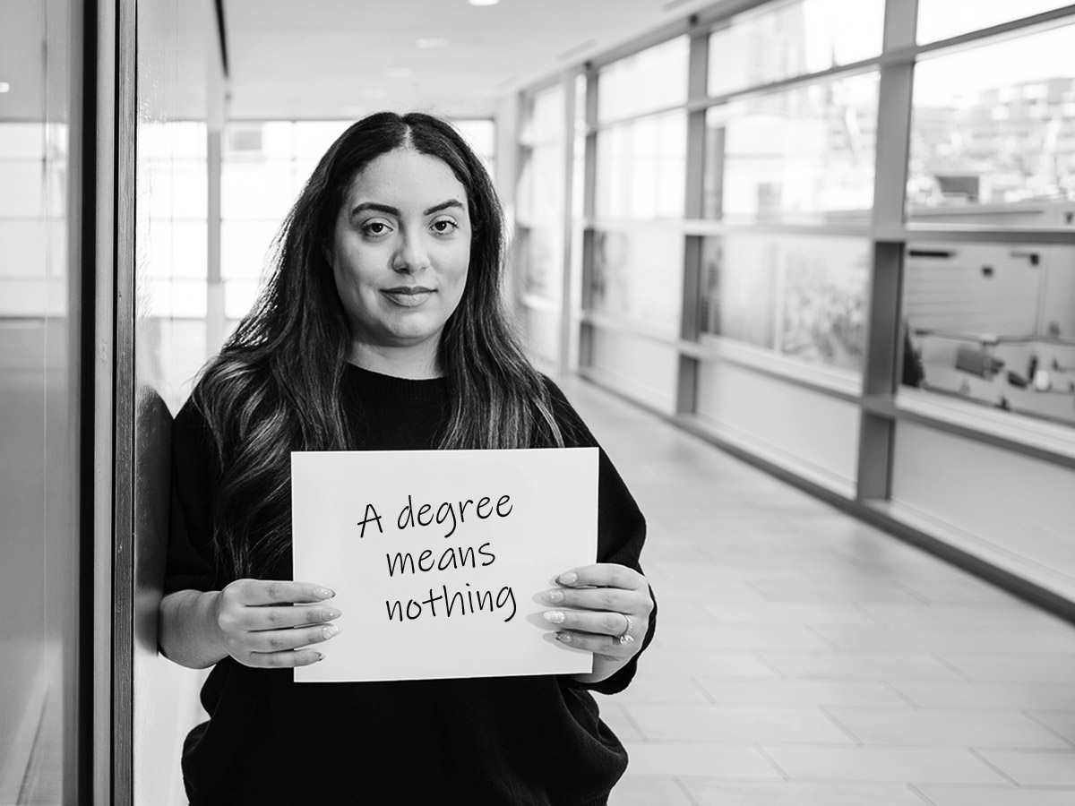Military spouse holding sign that reads "degrees mean nothing"